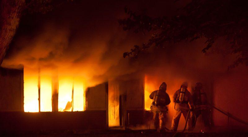 Brand i hus med brandmän framför.