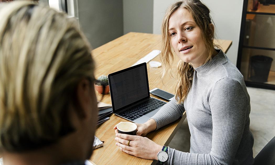 Kvinna med blont hår och i grå tröja tittar uppmärksamt på man med bakhuvudet mot kameran.