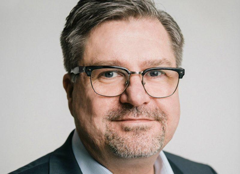 Ansiktsporträtt på Mikael Sjöberg - man med glasögon och gråsprängt hår och skägg.