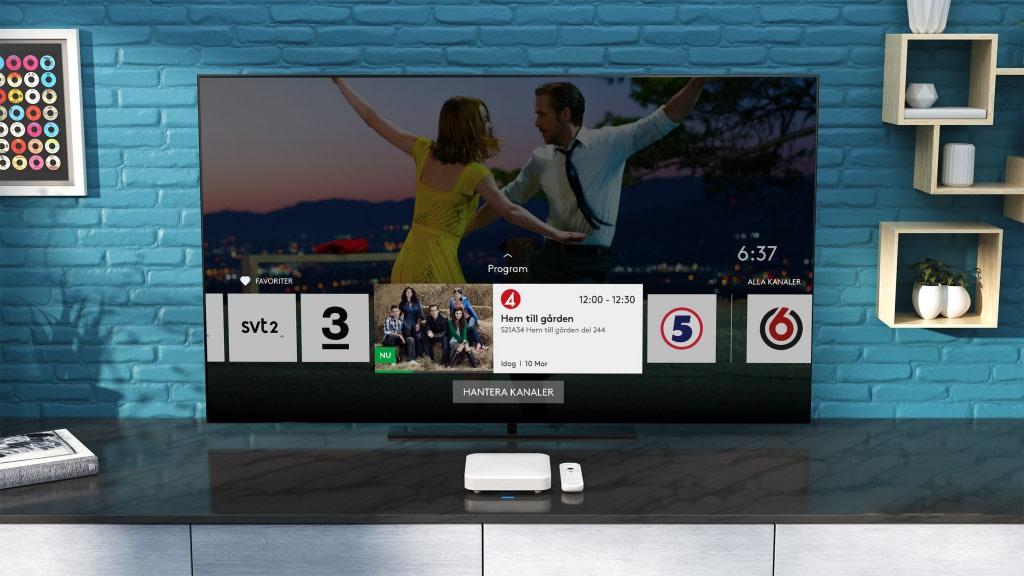 TV-skärm med kanalval över bord med vit box och fjärrkontroll.