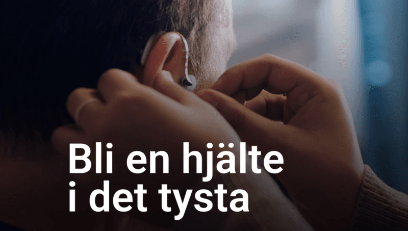 Händer sätter på en hörapparat på ett öra. Text: Bli en hjälte i det tysta.