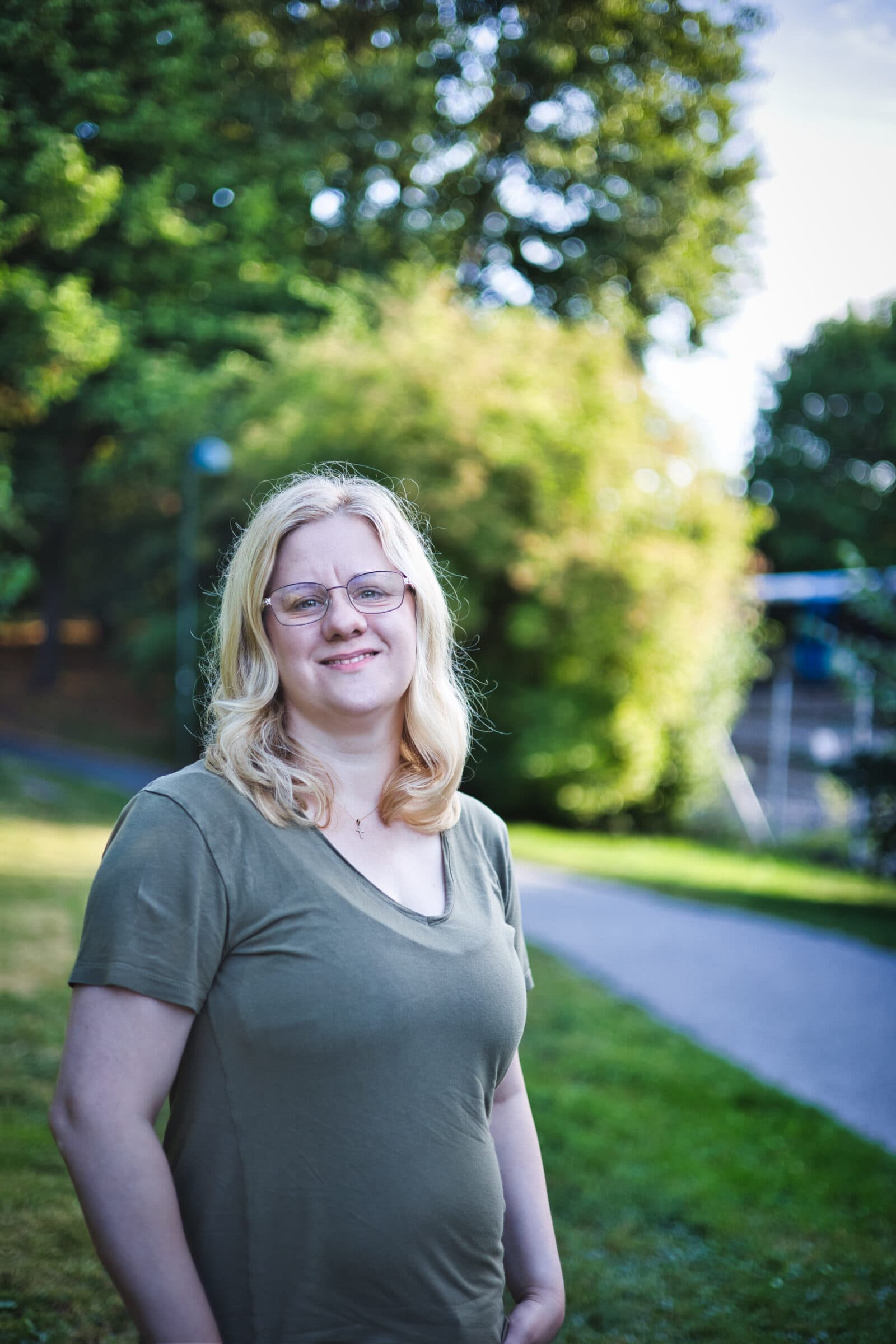 Bild på Lisa Carlbom, med en oskarp bakgrund, utomhus. Lisa har glasögon, blont hår och är klädd i en grön topp