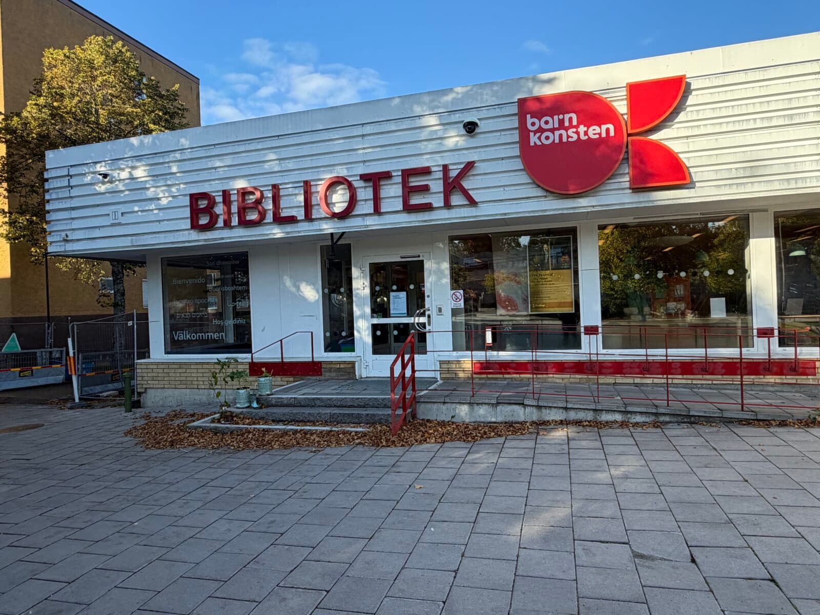 Bild på utsidan av Vårby bibliotek. Man ser entrén med en ramp för rullstol/barnvagn