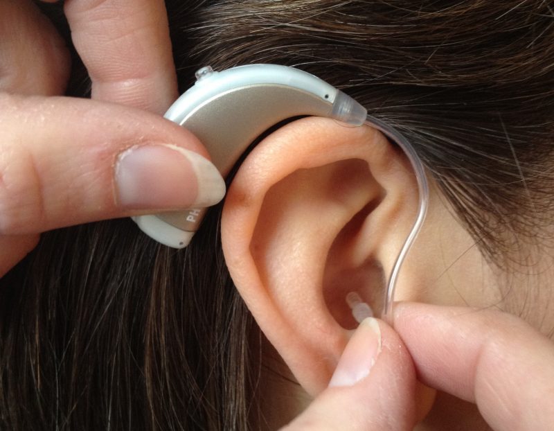 Fingrar sätter hörapparat på öra.