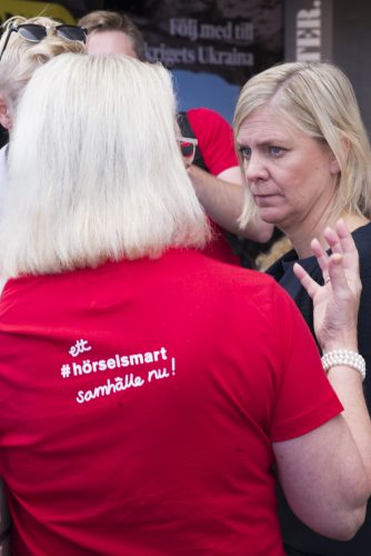 Magdalena Andersson syns bakom person med röf tröja med orden "Rtt hörselsmart samhälle nu!" 