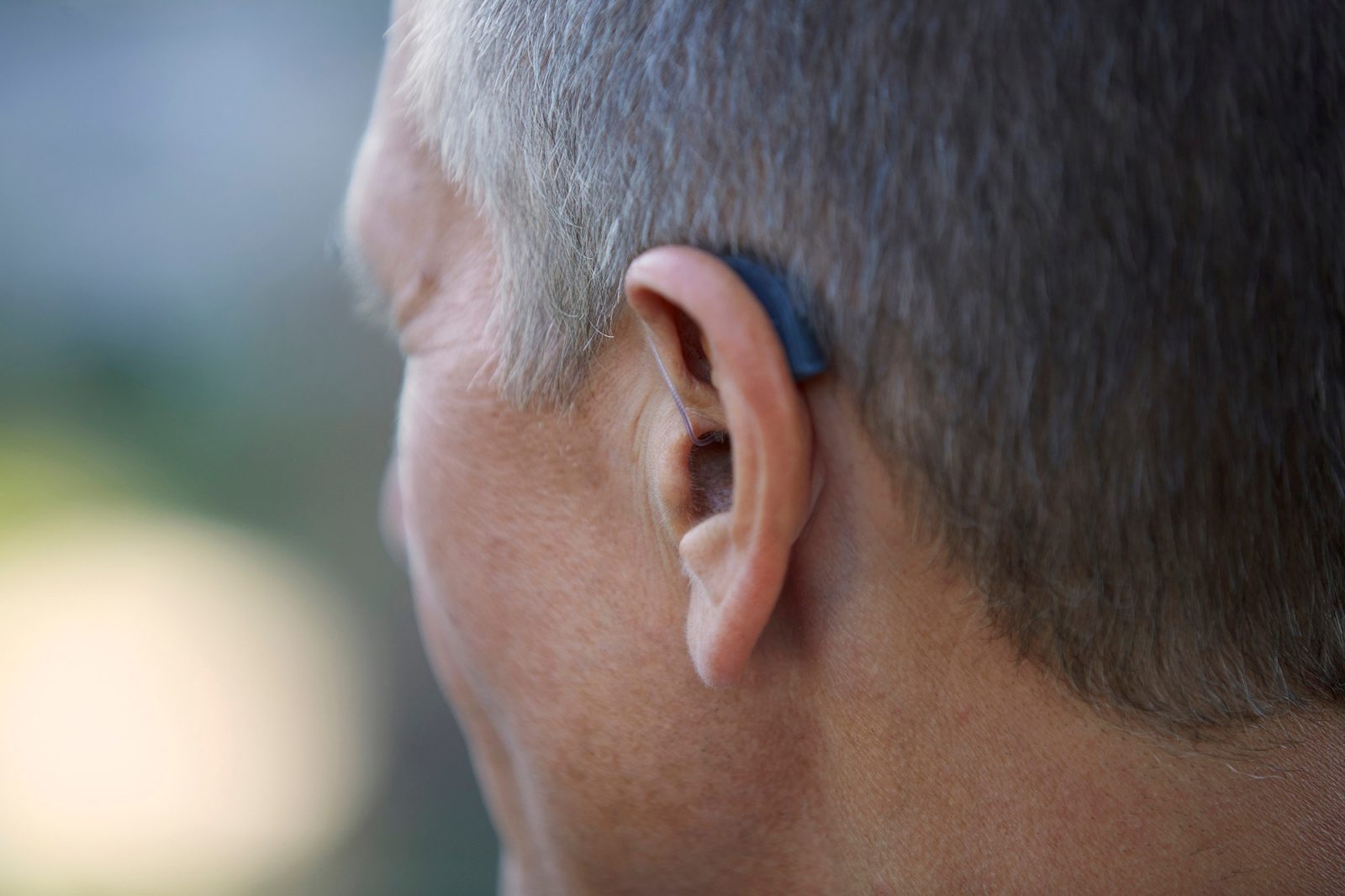 Medelålders man med hörapparat bakom örat sedd snett bakifrpn.