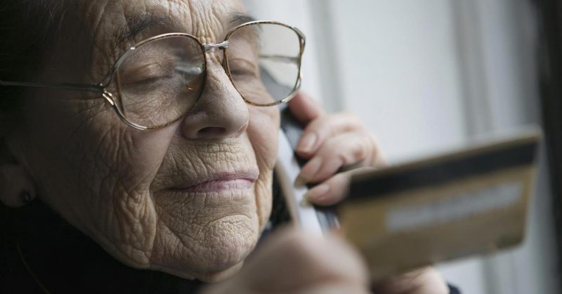Äldre person håller i telefonlur, tittar på kreditkort.
