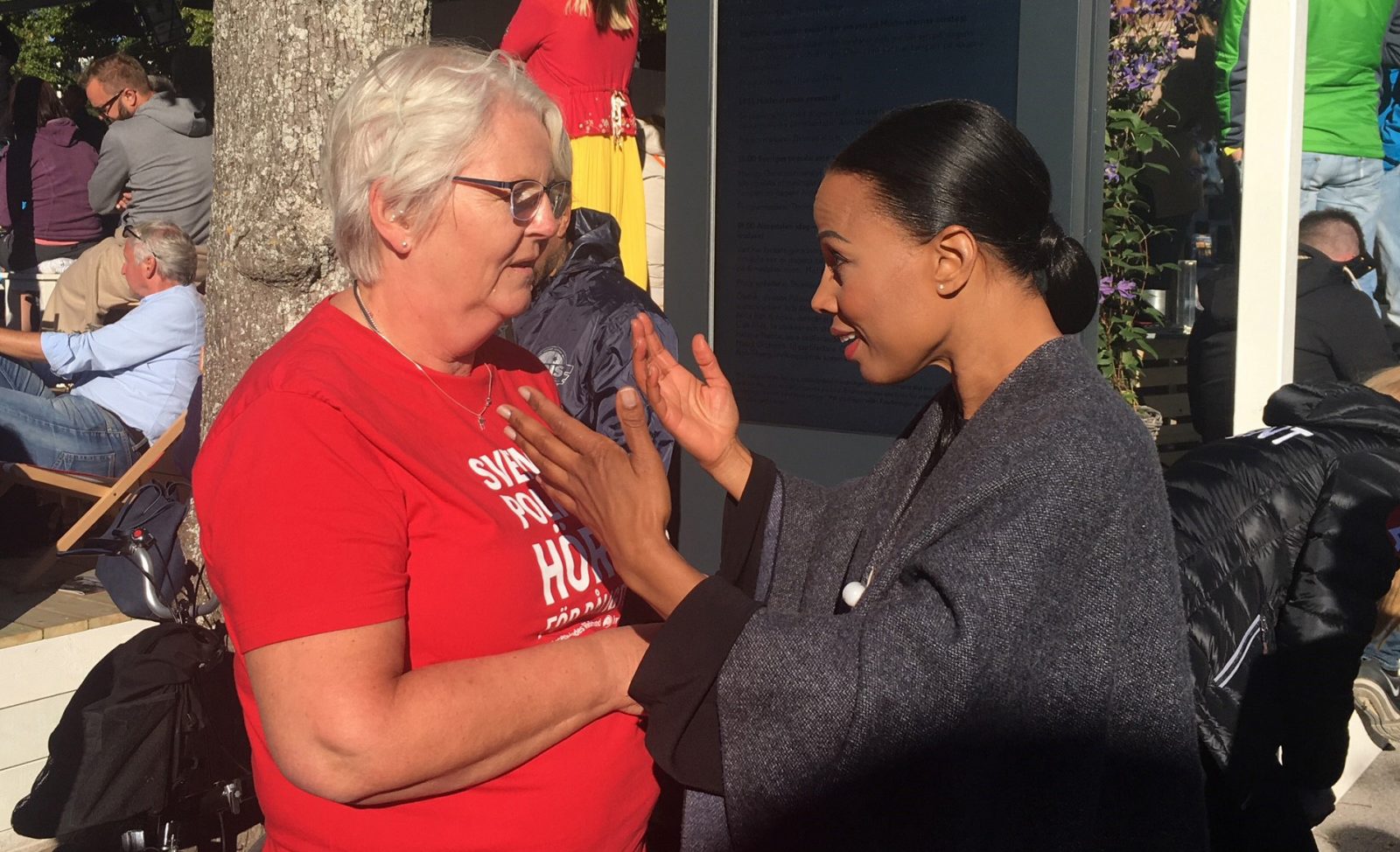 Kvinna i röd HRF-t-shirt pratar med kvinna som gestikulrerar.