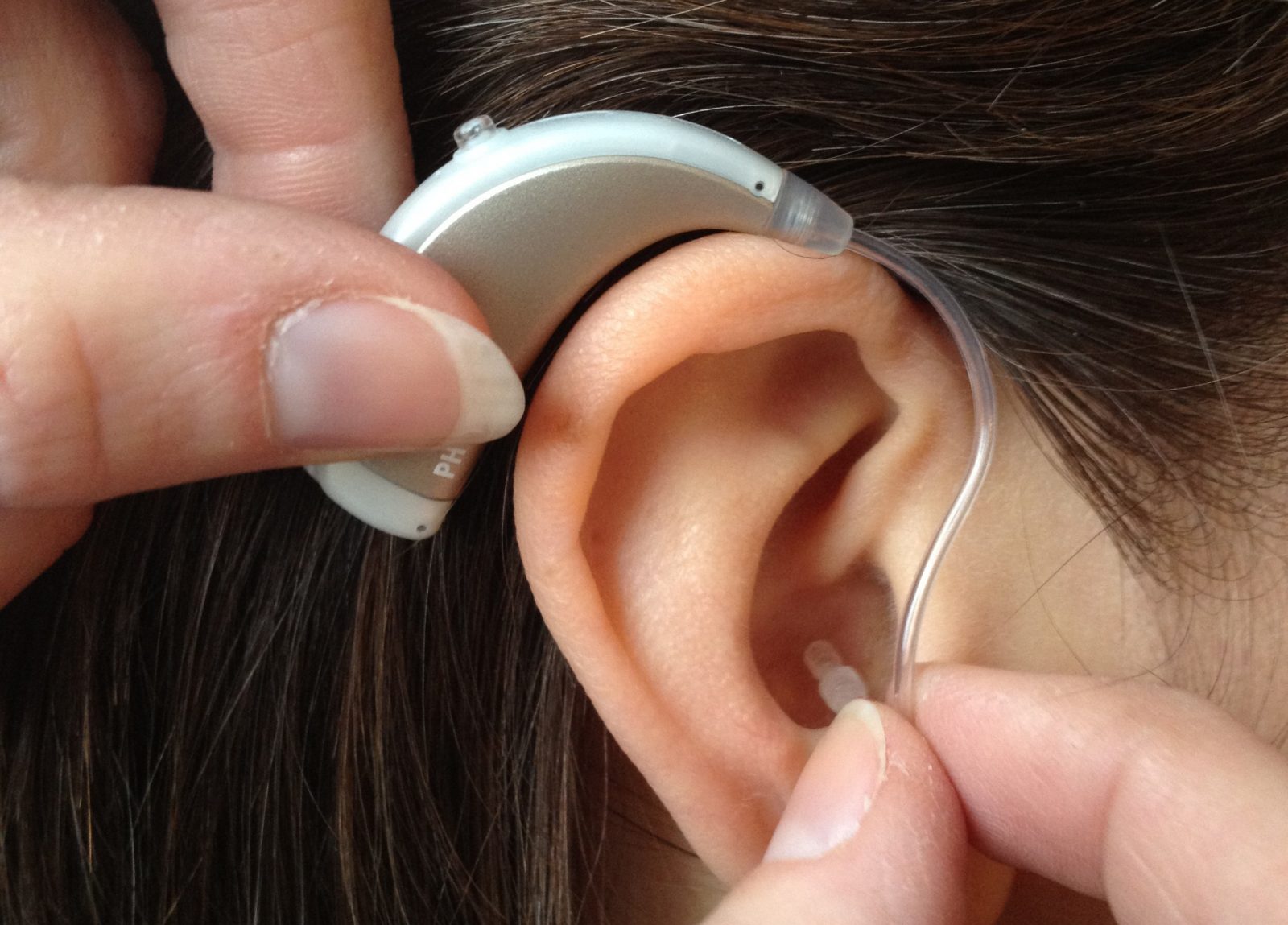 Fingrar sätter hörapparat på öra.
