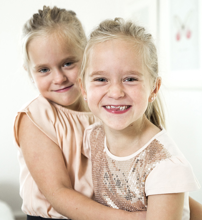 Två leende hörselskadade flickor med ljust hår.