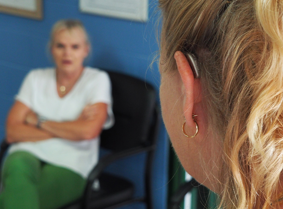 Kvinna med hörapparat sedd bakifrån samtalar med annan kvinna.