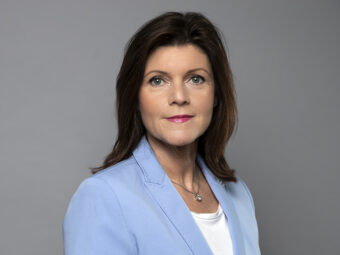 Porträtt på arbetsmarknadsminister Eva Nordmark med halvlångt mörkt hår, ljusblå kavaj och vit t-hirt.