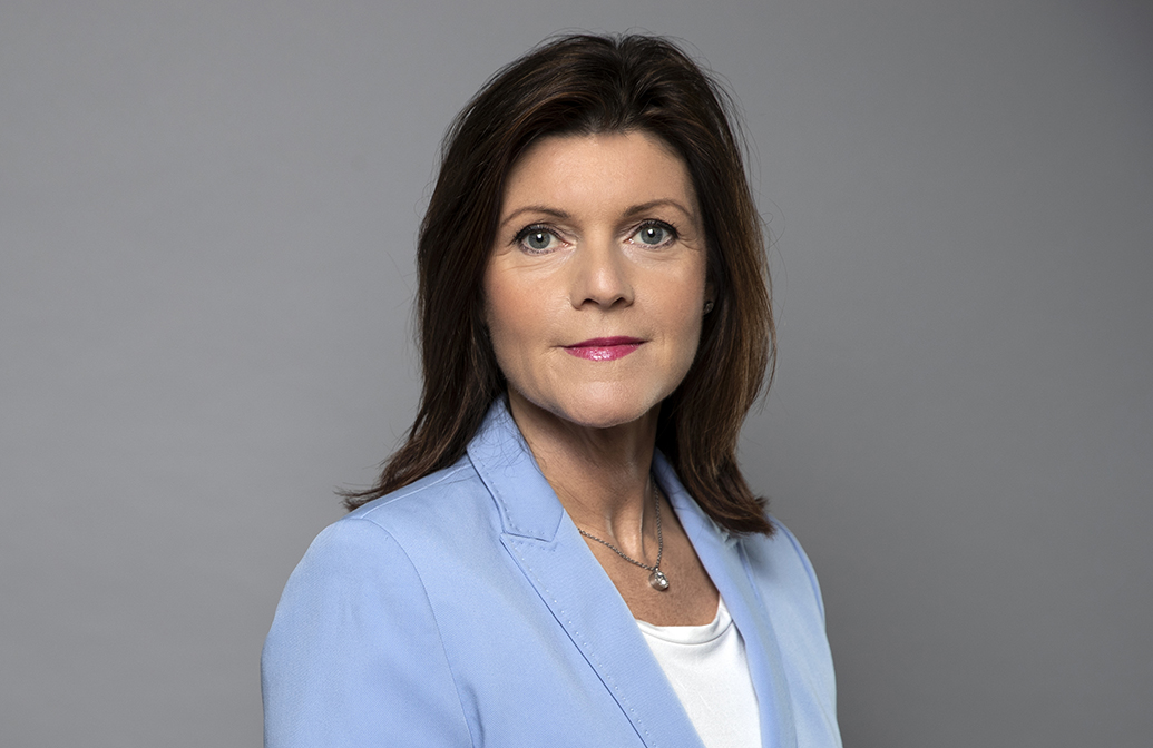 Porträtt på arbetsmarknadsminister Eva Nordmark med halvlångt mörkt hår, ljusblå kavaj och vit t-hirt.