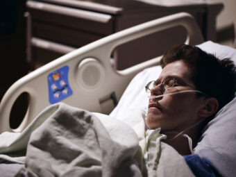 Kvinna med syrgasslang i näsan ligger i sjukhussäng.