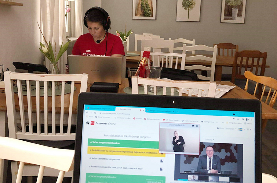 Laptop med kongressmöte i föregrunden. Kvinna i röd t-shirt i bakgrunden.-