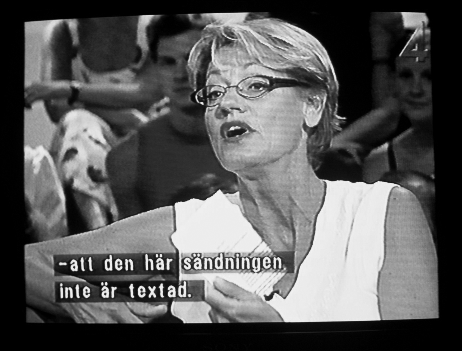 Svartvit bild på Gudrun Schyman i TV-ruta, med textremsa: "att den här sändningen inte är textad "