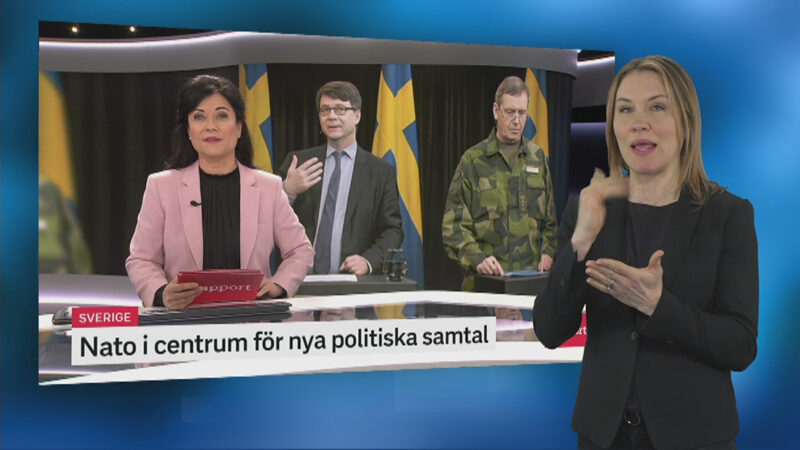teckenspråkstolk framför bild med nyhetsuppläsare på Rapport.