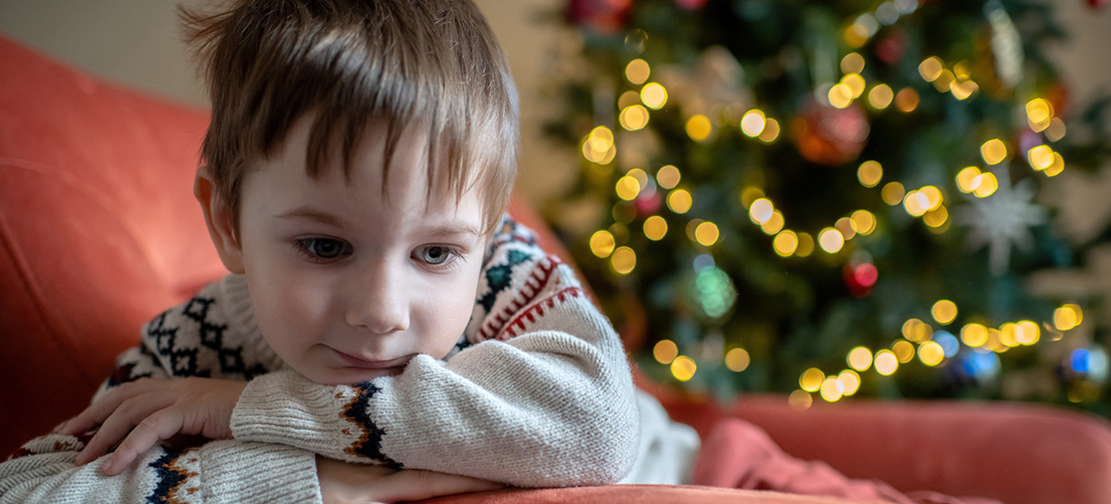 En tankfull pojke i närbild framför julgran.