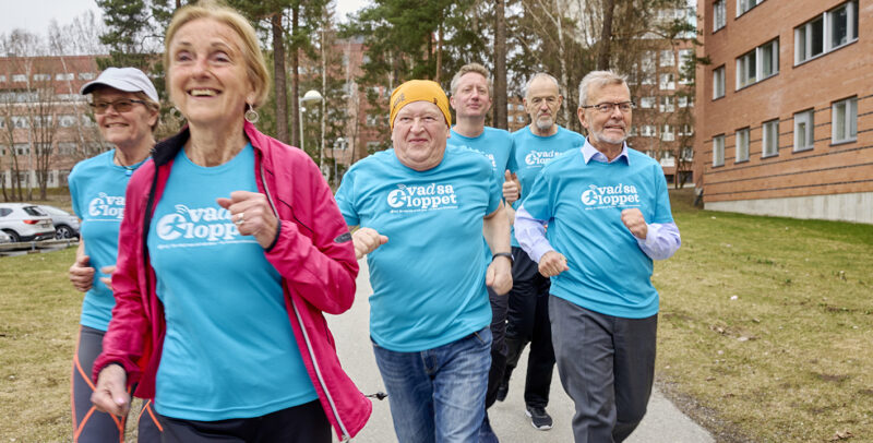 Grupp personer i blåa tröjor med Vad sa-loppet-logotyp springer leende mot kameran.