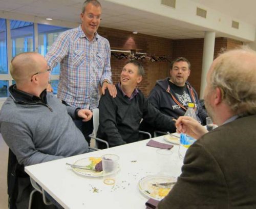 Glada människor står och sitter vid ett bord.